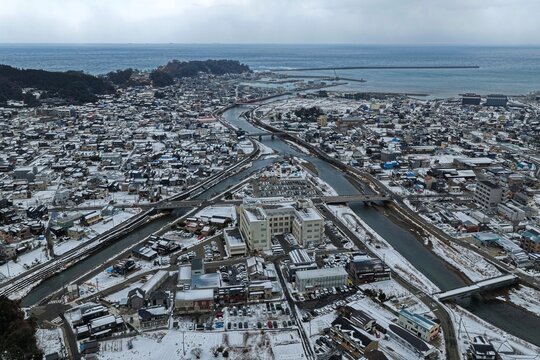 Aerial drone photo of snow-covered coastal town with river in Wajima, Ishikawa, Japan