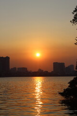 Fototapeta premium Sunset over calm lake water with city skyline background and golden light effect.