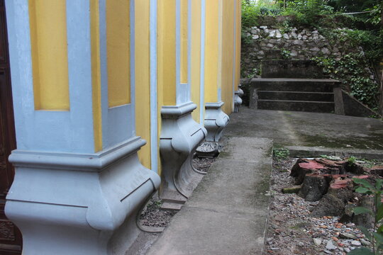 Yellow temple wall with blue concrete pillars and stairs leading to stone platform.