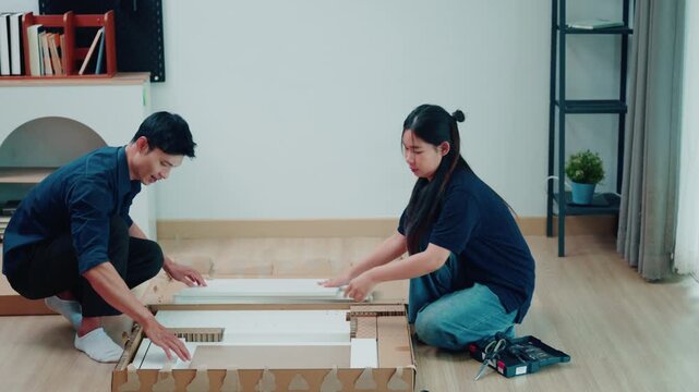 Asian Couple Assembling Flat Pack Furniture Together on Living Room Floor