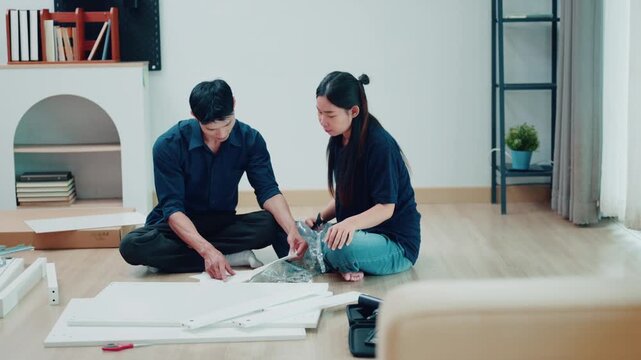 Asian Couple Assembling Flat Pack Furniture Together on Living Room Floor