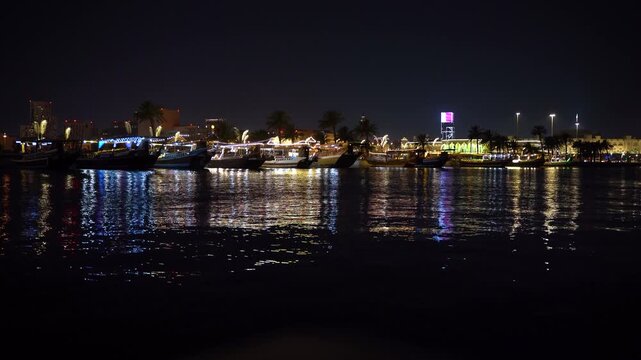 Night view of traditional dhow boats illuminated and docked at the Doha waterfront, with the city skyline in the background, Qatar.
