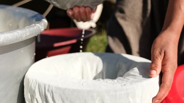 A woman first lines a container with cheesecloth, then transfers fresh cheese curd from a metal pot into the cloth to drain, showing traditional cheesemaking and rural dairy work in the highlands.