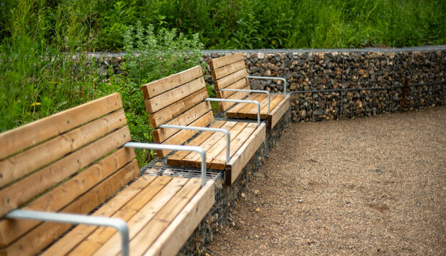 Three new modern wooden benches sitting in a park with a gravel walkway
