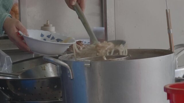 Close-up of a Person Preparing Banh Canh, Ladling Thick Rice Noodles and Broth into a Bowl at a Street Food Stall