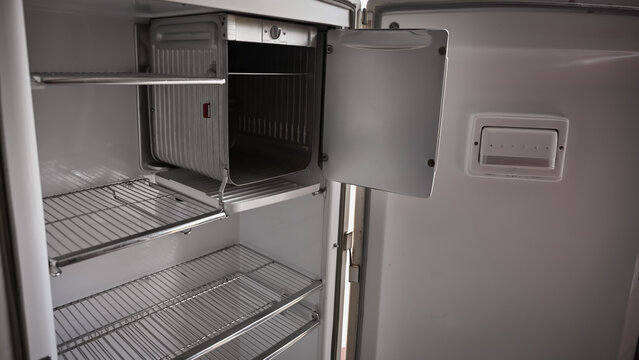 Interior of an empty vintage 1940s or 1950s white refrigerator with wire shelves and open freezer compartment.