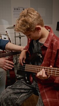 Vertical video of Caucasian young male music teacher instructing Caucasian teenage boy on playing bass guitar in studio. Clip for music school ads