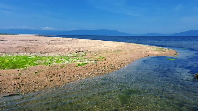 Beautiful panoramic view of a sandy beach spit surrounded by calm blue sea water under a clear summer sky