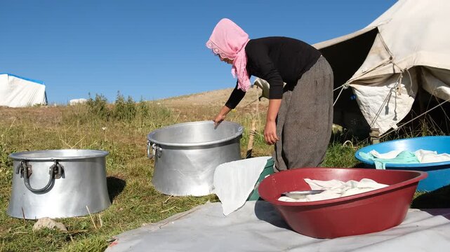 One woman pours fresh cheese curds from a large metal pot into a cloth-lined container outdoors, showing traditional cheesemaking, manual dairy work, and small-scale rural food production in sunlight.