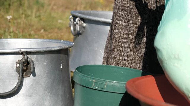 A woman transfers fresh cheese curds from a large metal pot into a cloth-lined container, showing traditional cheesemaking, manual dairy work, and small-scale outdoor food production outdoors by hand.