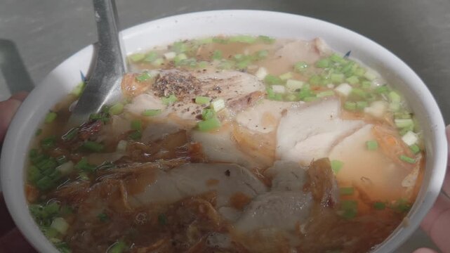 Close-up of a Bowl of Vietnamese Banh Canh Topped with Sliced Pork, Scallions, Fried Shallots, and Ground Pepper