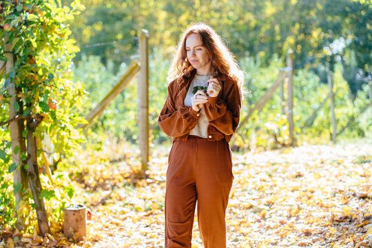 Thoughtful red haired woman enjoying quiet moment in warm sunny autumn orchard