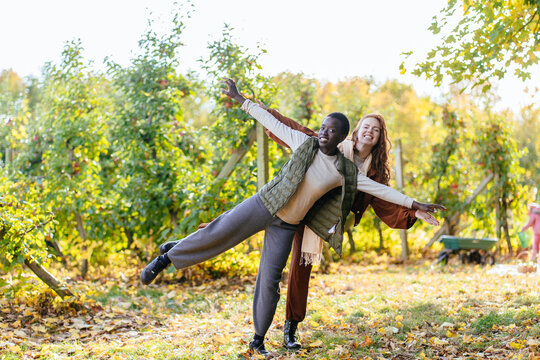 Playful diverse female friends balancing together during joyful autumn orchard adventure