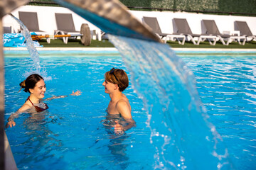 Naklejka premium Happy young couple swimming in a luxury resort pool and talking together.