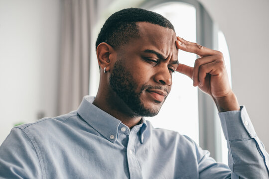 Young adult man gripping his forehead tightly, expressing intense pain and frustration from a severe headache, migraine, or overwhelming stress, showcasing struggle and discomfort