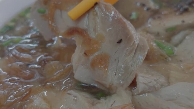 Close-up of Using Chopsticks to Lift a Piece of Sliced Pork from a Bowl of Vietnamese Banh Canh