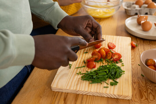 African American couple cooking, slicing cherry tomatoes with chef knife and mixing eggs in kitchen