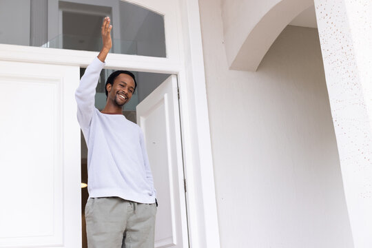 African American man standing at front door with transom, waving, wearing light pullover and khakis