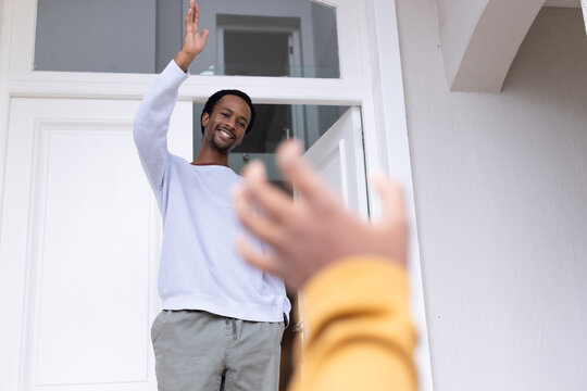 African American father waving and smiling in front door with transom window, teenage son reaching