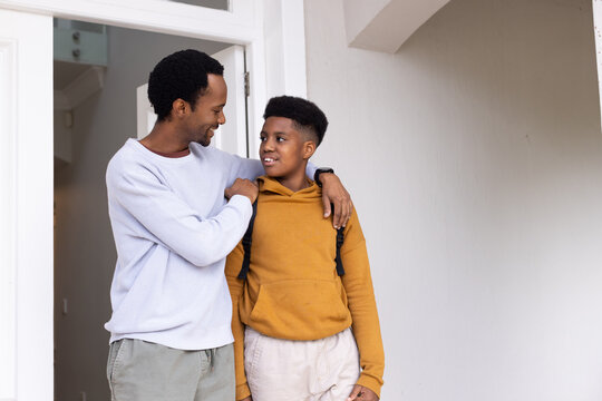Father and teenage son standing in doorway, talking while showing backpack straps and wristwatch