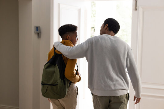 African American father, teen son standing in foyer, sweater, hoodie, backpack, open door, keypad