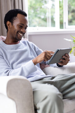 African American man sitting in living room chair, holding tablet in folio case and tapping screen