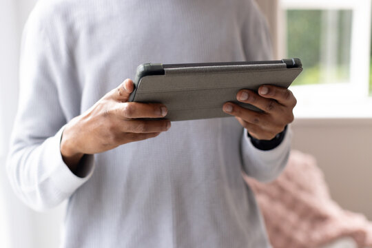 African male holding tablet in landscape at home, wearing light grey ribbed top and smartwatch