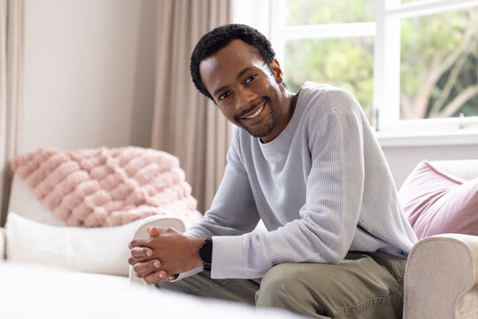 African American man smiling leaning forward on sofa in living room with pink throw and smartwatch