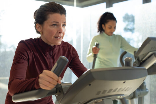 African American women exercising on ellipticals at gym, wearing maroon and mint tops with console