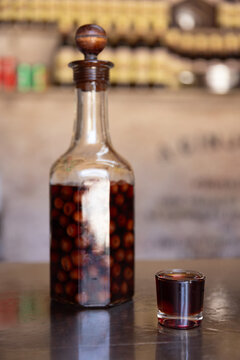 Clear bottle of infused and preserved cherries for ginja, ginjinha, traditional Portuguese cherry liqueur, next to a pour. 