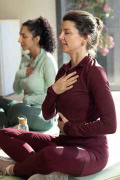 Two women sitting breathing mindfully on mats, one wearing burgundy set, cork-cap bottle nearby