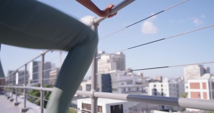 Woman in headband starting rooftop warmup stepping on railing, stretching legs, checking smartwatch