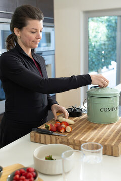 Woman wearing black zip-up jacket chopping strawberries on butcher-block cutting board near COMPOST