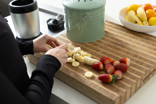 Woman slicing banana using knife on striped board at kitchen counter wearing longsleeve black top