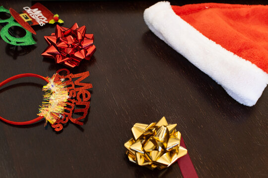 Santa-style hat is resting on dark wood table, with red bow, gold bow, green glasses
