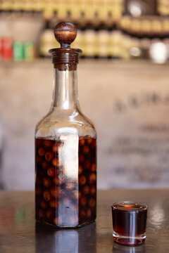 Clear bottle of infused and preserved cherries for ginja, ginjinha, traditional Portuguese cherry liqueur, next to a pour. 