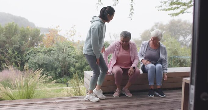Diverse women on deck mature woman walking to bench helping seniors adjusting shoes getting up