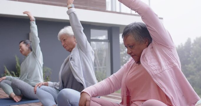 Diverse women following right woman doing seated side stretch on mats in gear on deck exercising
