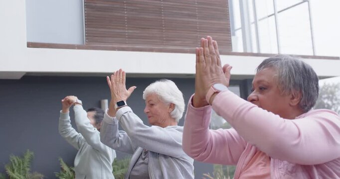 Diverse female friends following leader cue, lowering arms into prayer while centering on yoga mats