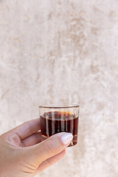 female hand holding a shot of Ginja - portugese cherry liqueur against a textured wall, copy space