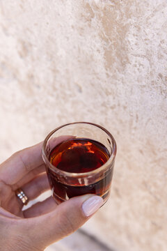 female hand holding a shot of Ginja - portugese cherry liqueur against a textured wall, copy space