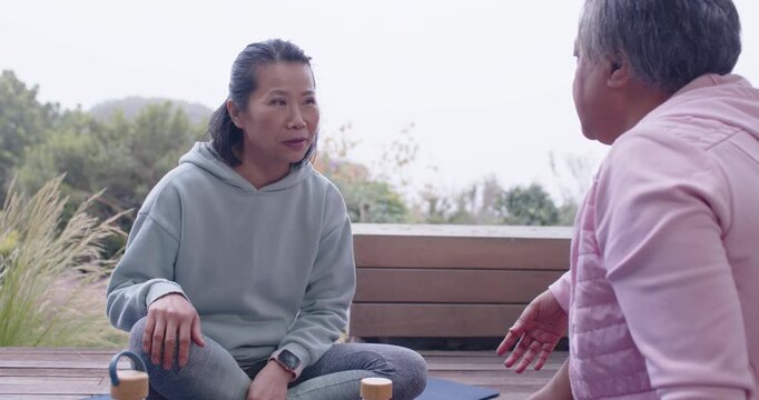 Diverse women Asian woman in hoodie replying to gestures talking and tapping smartwatch on deck