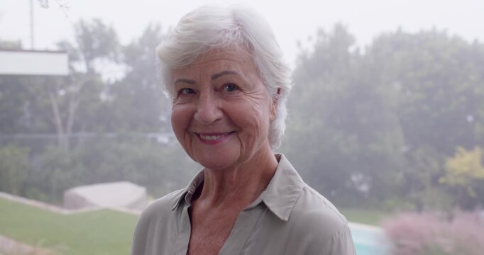 Senior woman in collared shirt, smiling, turning while camera moving closer by glass wall over pool