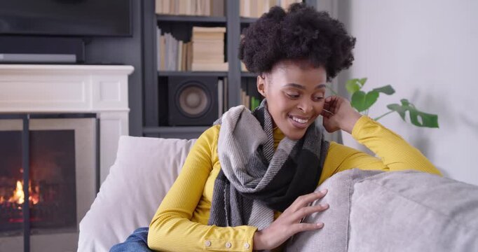 African American woman responding to camera, adjusting scarf, touching sofa, smiling in living room