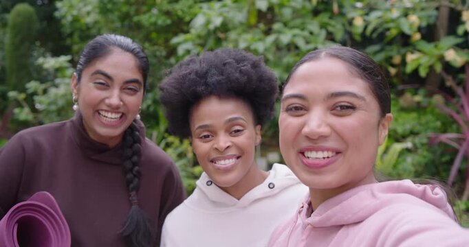 Diverse women with mat, right woman raising phone in garden filming selfie and laughing together