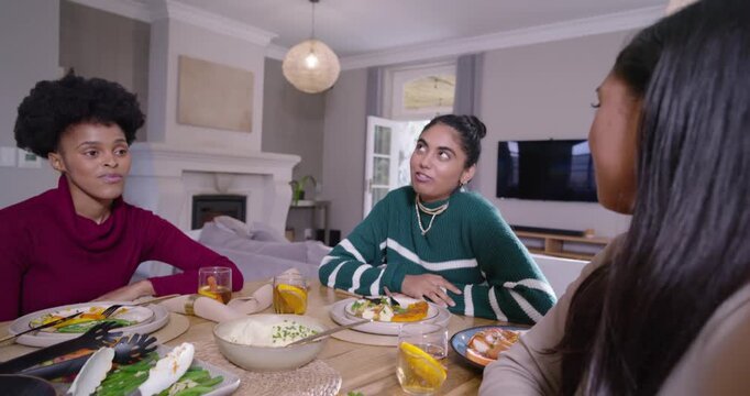 Diverse women friends right woman leaning in, smiling, middle cutting food and toasting at table
