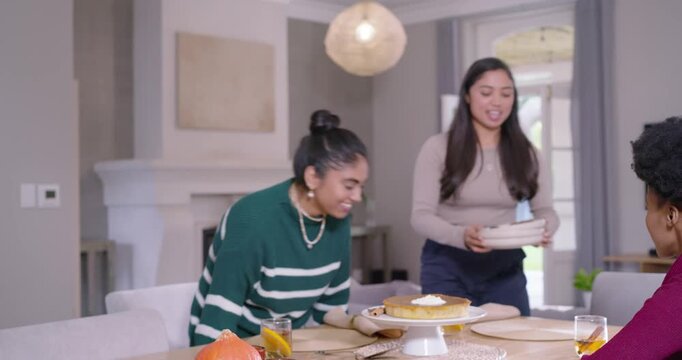 Diverse females watching green top placing cake, tan sweater host serving slice for party at table