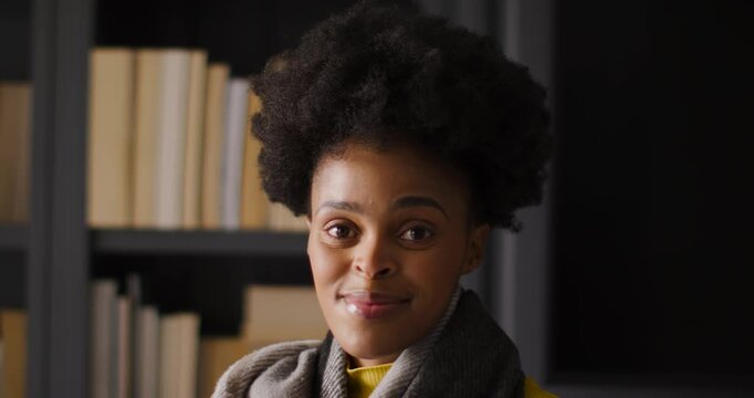 African American woman smiling tilting head responding to cue in room with bookshelf and yellow top