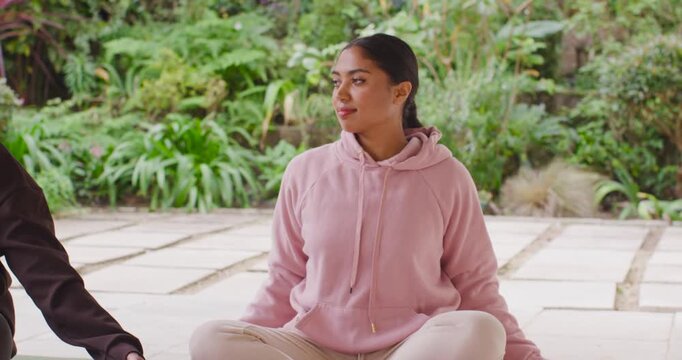 Adult African American woman sitting on pink-mat after cue lifting hands for prayer in pink hoodie