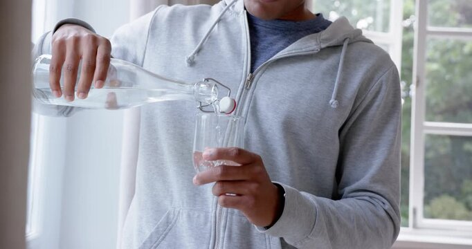 Man in his 20s lifting swing-top bottle, pouring water into glass at home to hydrate